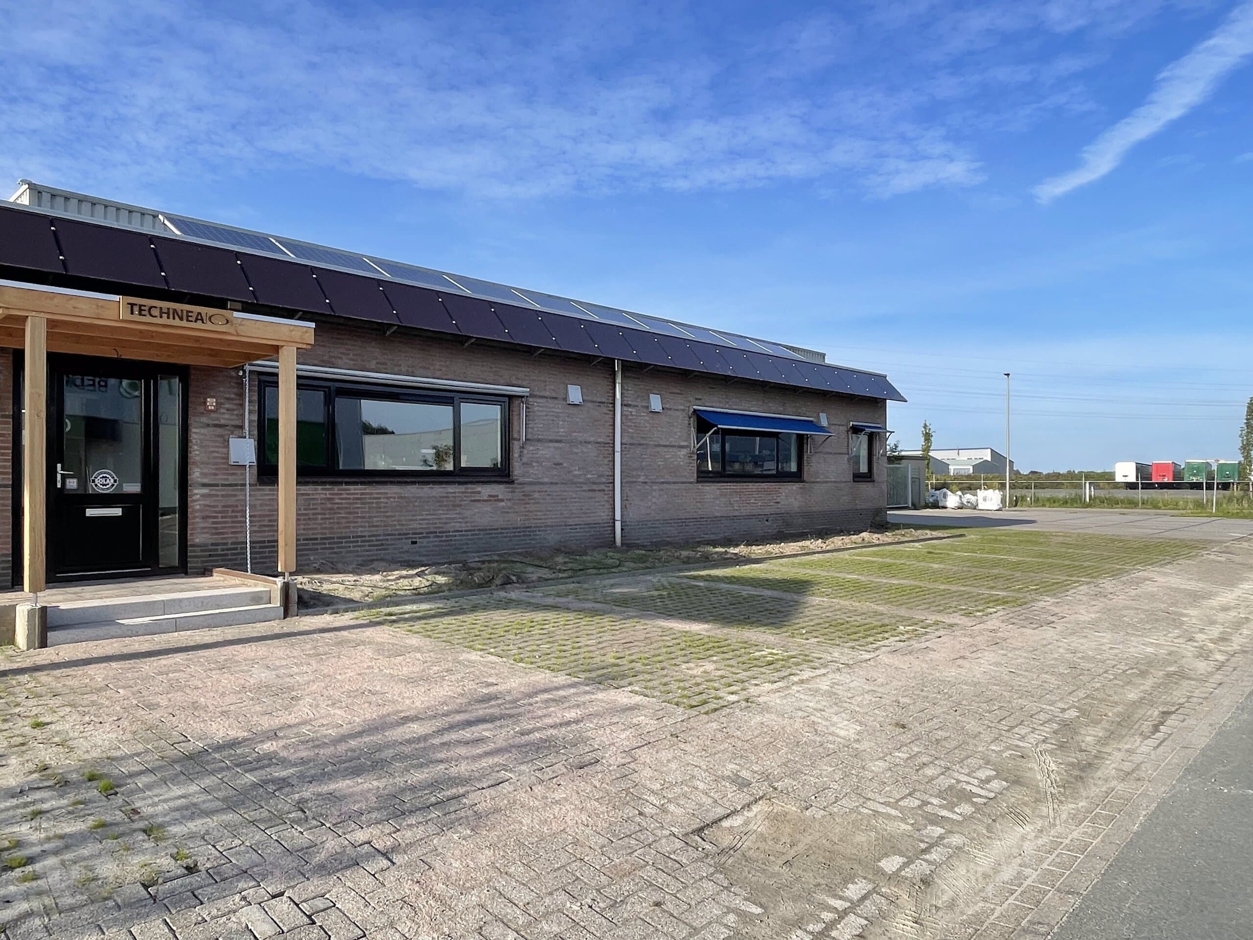 Bedrijfspand met zonnepanelen op het dak en een parkeerterrein van grasbetonstenen, met een pas ingezaaide grasstrook langs de gevel