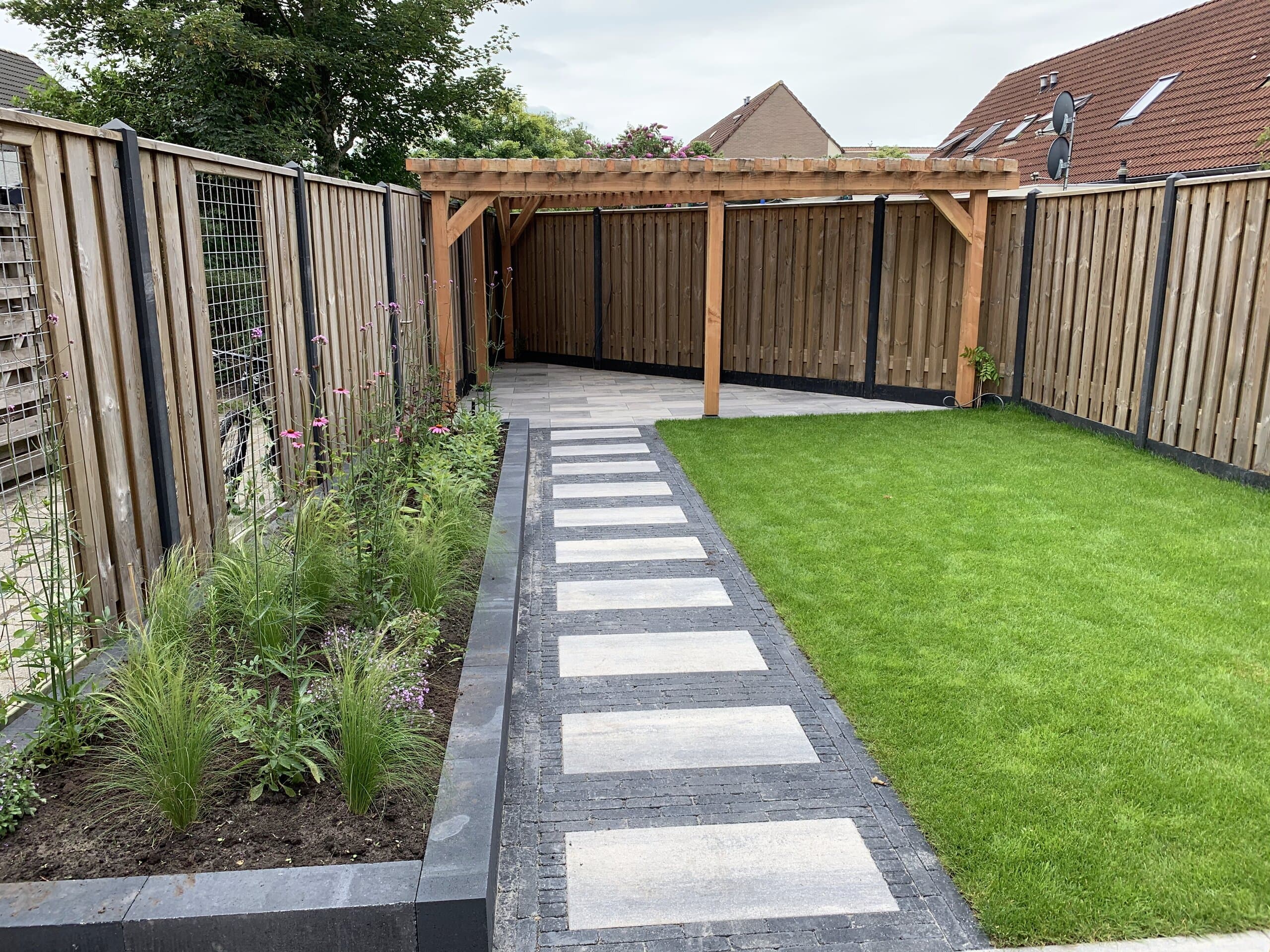 Aangelegde achtertuin met een houten pergola, een pad van lichte tegels in donkere klinkers, een strak gazon en een border met siergrassen en roze zonnehoed